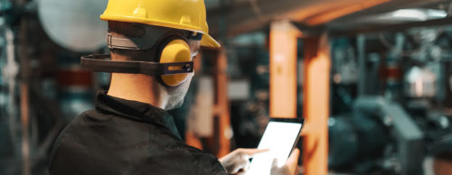 Worker with headphones and hard hat consults tablet